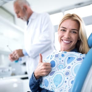person giving a thumbs-up while sitting in a dentist’s chair