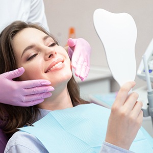 Woman smiling in mirror after cosmetic dental treatments