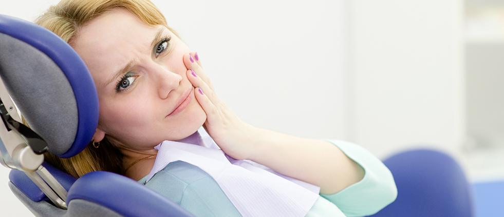 Woman in dental chair holding cheek before tooth extractions