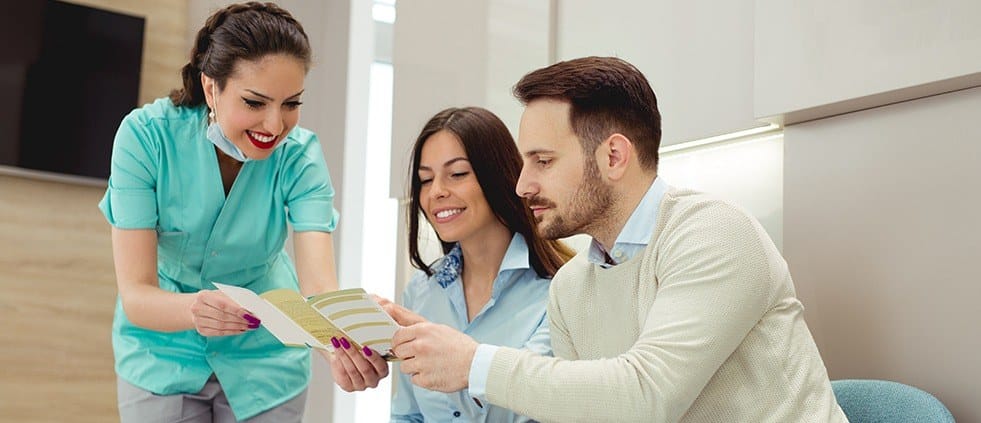 Dental team member talking to two dental patients about dental insurance