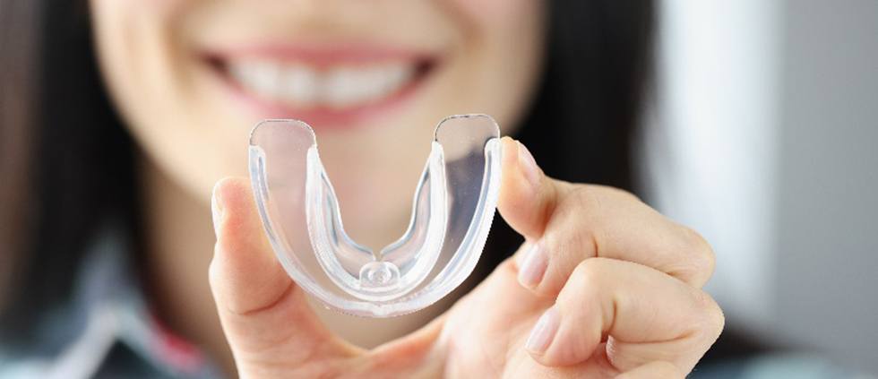 Woman smiling while holding clear nightguard in Lincoln 