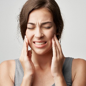 Closeup of woman in grey shirt struggling with jaw pain