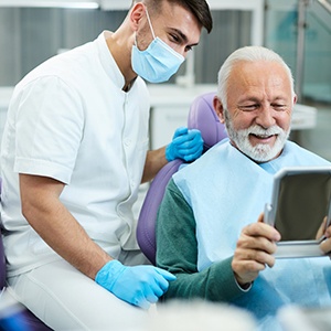 Senior dental patient holding mirror and smiling