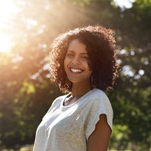 A woman wearing a gray shirt and standing outside, smiling and pleased with the results from her root canal