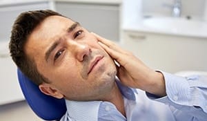 Man in dental chair holding jaw before emergency dentistry