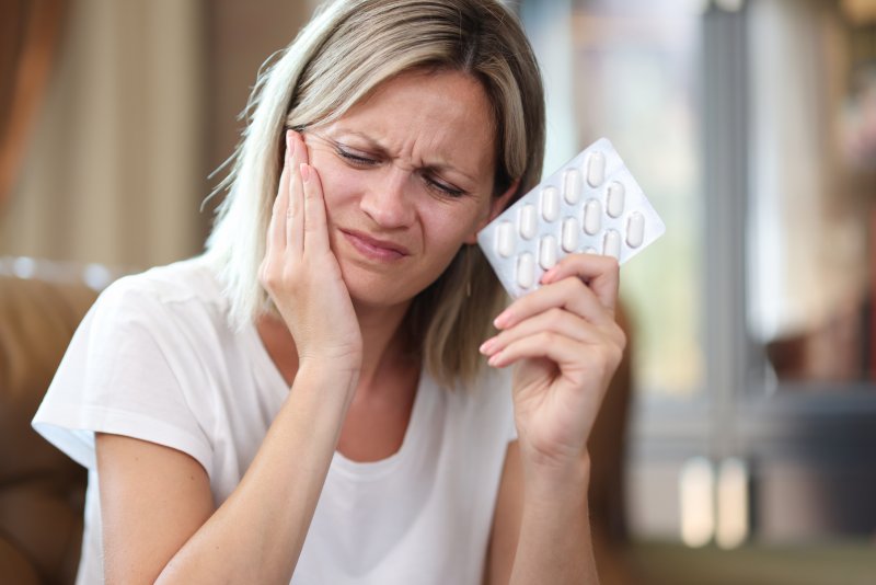 A woman holding her jaw in pain about to take antibiotics before her dental visit