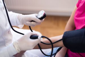 Medical staff wearing white gloves taking blood pressure of woman in pink shirt